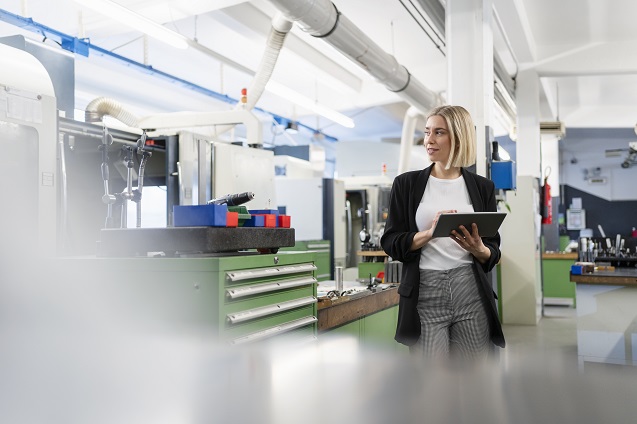 Woman holding tablet in factory hall looking around